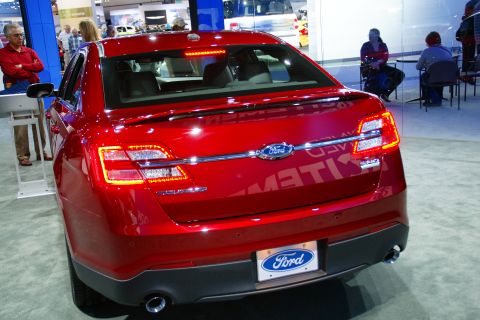 1993 Ford Taurus - Red Ford sedan at an auto show, likely a later model than claimed.