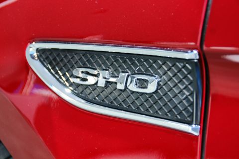 1993 Ford Taurus - Close-up of a red car's fender, highlighting the chrome SHO badge against a textured black grille.