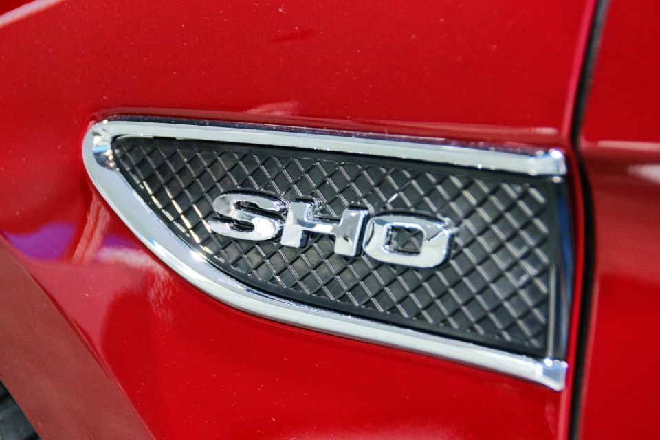 Close-up of a red car's fender with a chrome SHO badge on a black grille insert