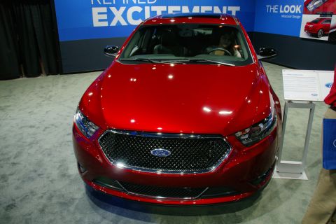 1993 Ford Taurus - A red Ford sedan is displayed at an auto show with informational placards nearby.