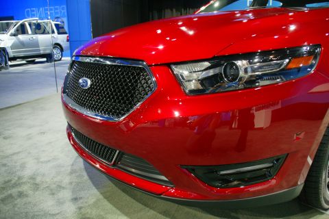 1993 Ford Taurus - A red Ford sedan is displayed at an auto show, with a silver SUV in the background.