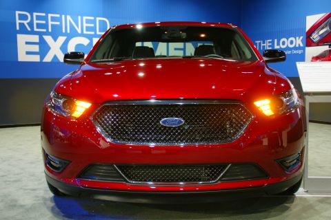1993 Ford Taurus - Red Ford sedan with a distinctive grille and front lighting at an auto show.