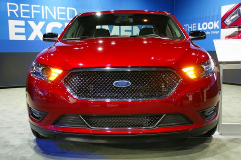 1993 Ford Taurus - A red Ford sedan is displayed at an auto show with promotional text in the background.