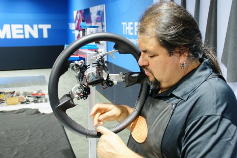 1993 Ford Taurus - A man meticulously works on a steering wheel at a display, with text visible in the background.