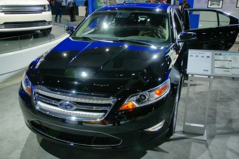 1993 Ford Taurus - A black Ford Taurus is displayed at an auto show with its driver's door open and information placards nearby.