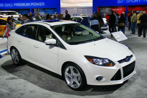 1993 Ford Taurus - A white Ford Focus sedan is displayed at an auto show with people in the background.