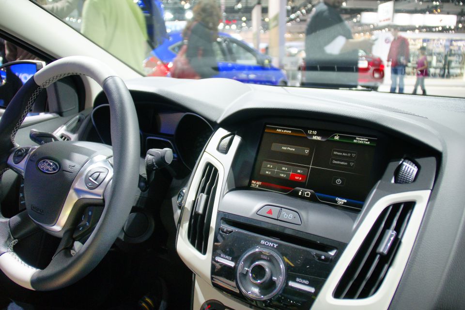 Car interior showing steering wheel, dashboard, and infotainment screen. The screen displays phone and navigation options