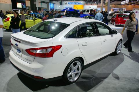 1993 Ford Taurus - A white Ford sedan is displayed at an auto show with other vehicles in the background.