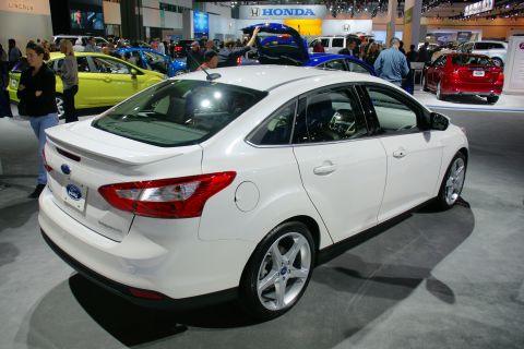 1993 Ford Taurus - A white Ford sedan is displayed at an auto show, with other vehicles and attendees in the background.