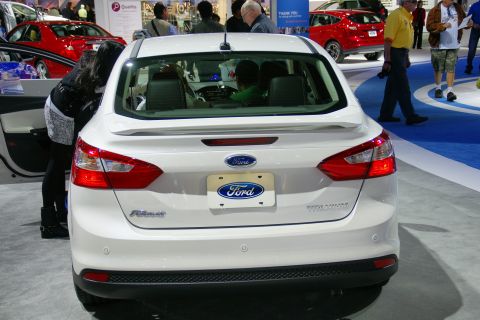 1993 Ford Taurus - A white Ford sedan is displayed at an auto show, with other vehicles and attendees visible in the background.