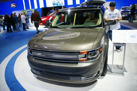 1993 Ford Taurus - A Ford Flex is displayed at an auto show, with people around and other vehicles in the background.