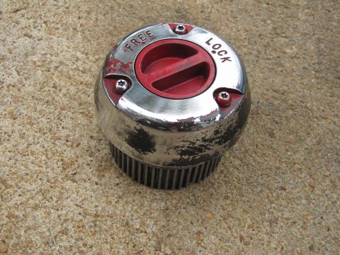 1995 Ford Bronco - A close-up of a worn chrome and red free-lock hub, indicating its function for vehicle wheel engagement.