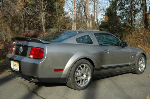 2008 Ford Mustang - Rear quarter view of a gray 2008 Ford Mustang Shelby GT500 with black racing stripes and a rear spoiler.