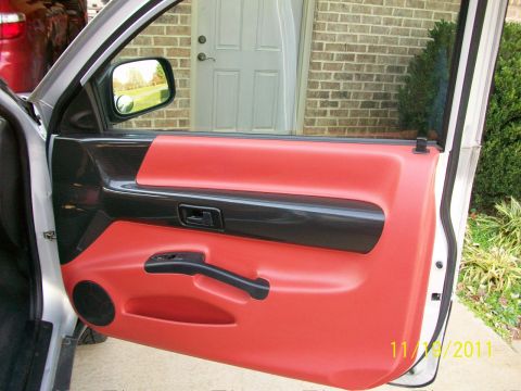 1999 Isuzu Vehicross - The interior door panel features red upholstery and black trim accents, with a side mirror reflecting an outdoor scene.