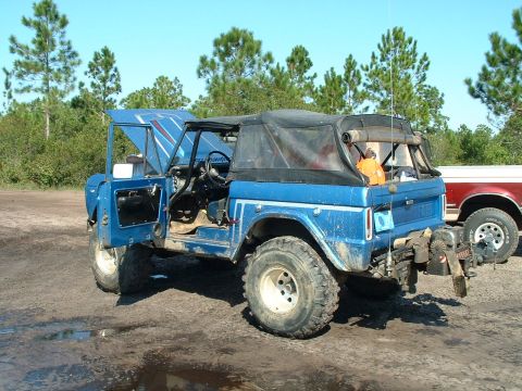 1995 Ford Bronco - A blue Ford Bronco sits in a muddy lot with its hood and doors open, ready for off-road adventure.