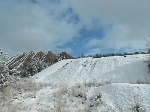 1979 Ford Bronco - Tire tracks mark a snowy hill with distant mountains under a cloudy sky.