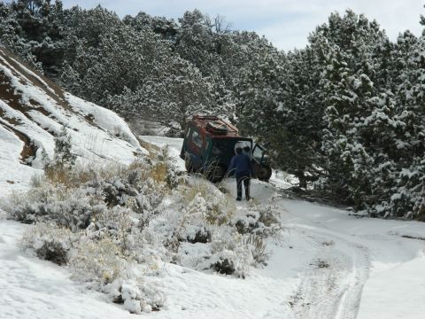 1979 Ford Bronco - A vehicle is stuck on a snowy, wooded trail with a person standing next to it.