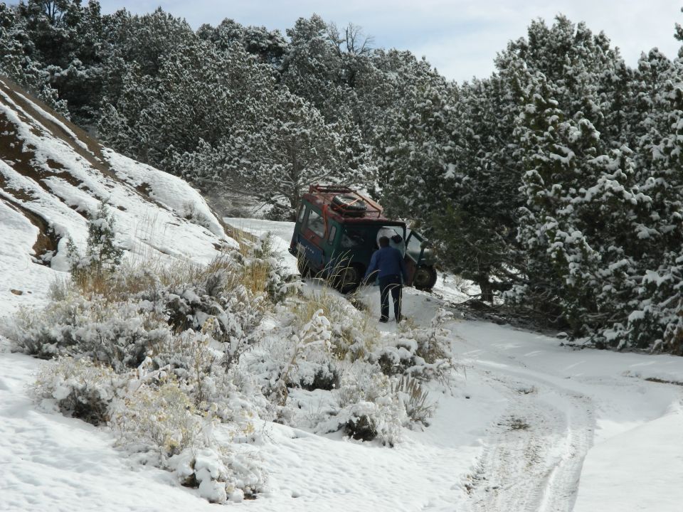 Off-road vehicle with open door stuck on snowy trail, person standing nearby