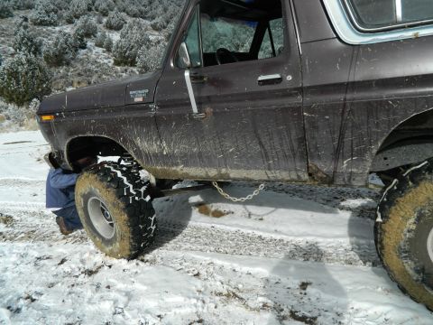 1979 Ford Bronco - 1979 Ford Bronco with large tires in snow, someone working on front wheel.