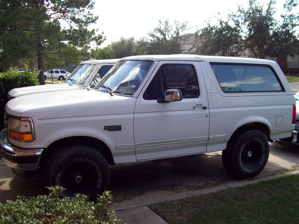 White Ford Bronco SUV side view in driveway with black wheels and large Pathfinder tires