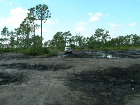 1995 Ford Bronco - A white SUV navigates a challenging muddy off-road course under a partly cloudy sky.