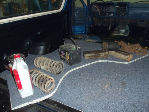 1985 Ford Bronco - Vehicle interior with suspension springs, battery, and tools laid out on the carpeted floor.