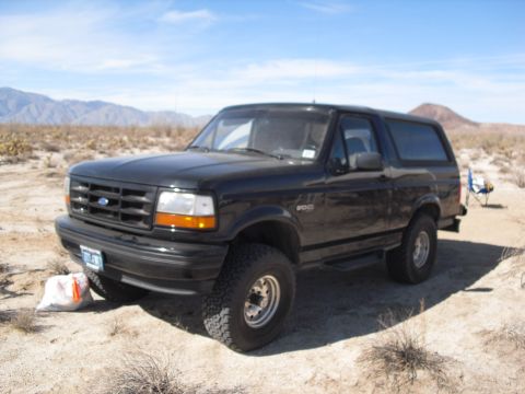 1986 Ford Bronco - This black Ford Bronco SUV is parked in a dry, desert-like environment under a clear blue sky.