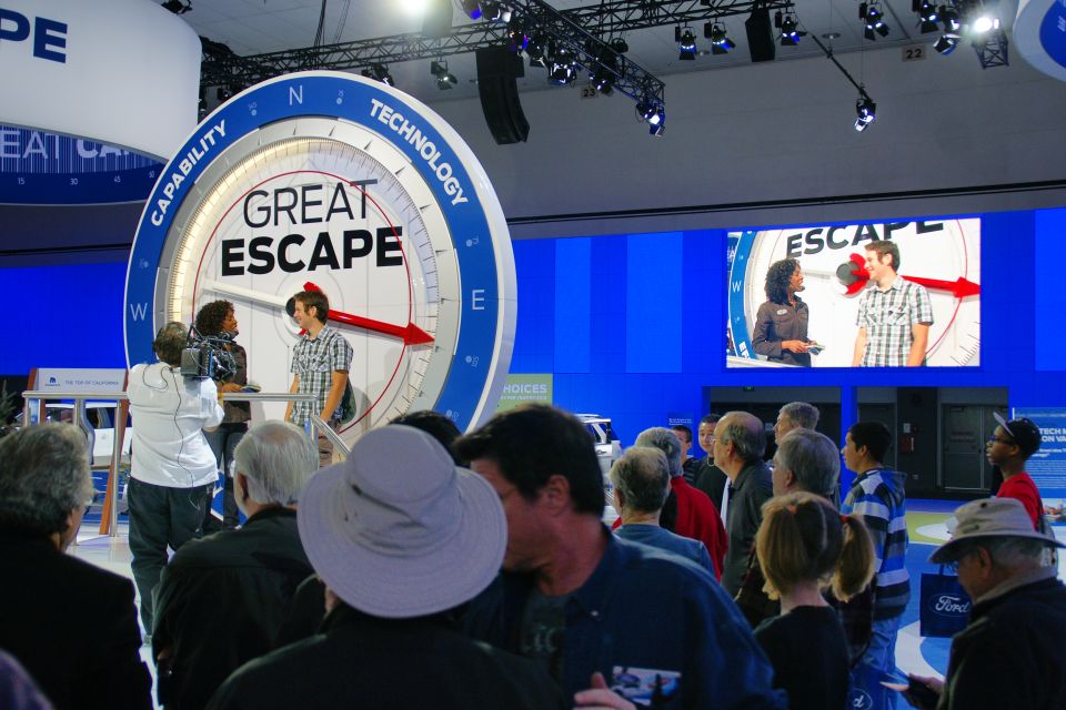 Auto show display a large compass-like graphic with 'GREAT ESCAPE' and people watching