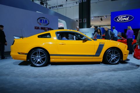 1993 Ford Taurus - A yellow Ford Mustang Boss 302 is displayed at an auto show next to a Ford logo.