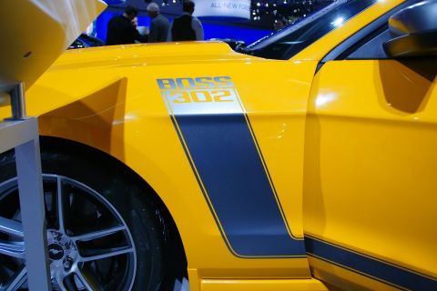 1993 Ford Taurus - A yellow car with blue racing stripes and "BOSS 302" badging is displayed at an auto show.