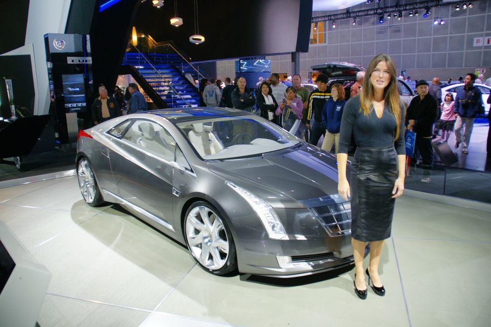 Gray coupe concept car with a woman standing next to it at an auto show