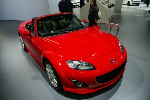 1993 Ford Taurus - A red Mazda Miata convertible is shown at an auto show with people in the background.