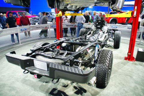 1993 Ford Taurus - Chassis of a Ford F-150 Raptor is displayed at an auto show, with other vehicles in the background.