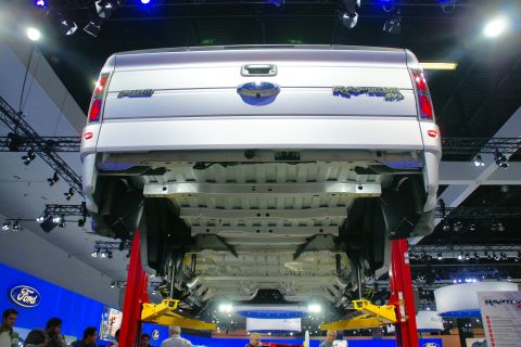 1993 Ford Taurus - Silver Ford F-150 Raptor pickup truck displayed on a lift at an auto show, viewed from the rear.