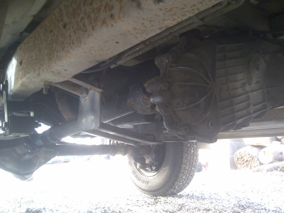 Underside view of a vehicle's transmission and driveshaft, with a tire visible