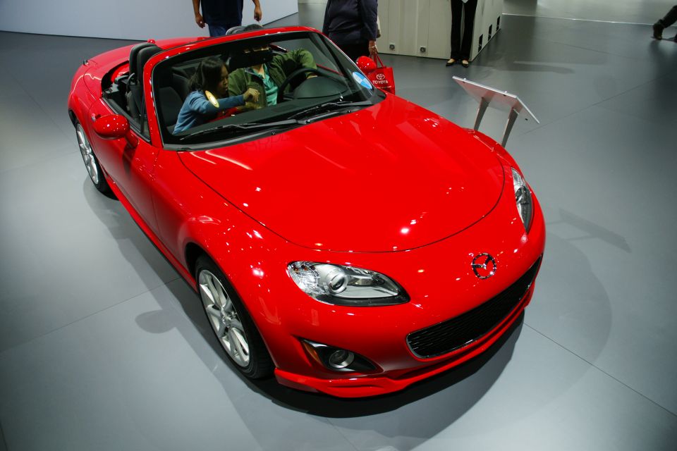 Red convertible sports car with black interior. Two people are visible inside