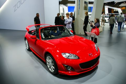 1993 Ford Taurus - A red convertible sports car is displayed at an auto show with people in the background.