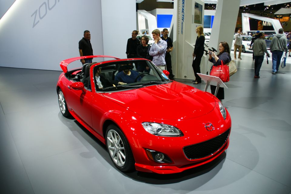 Red convertible sports car with a spoiler, viewed from the front-right at an auto show