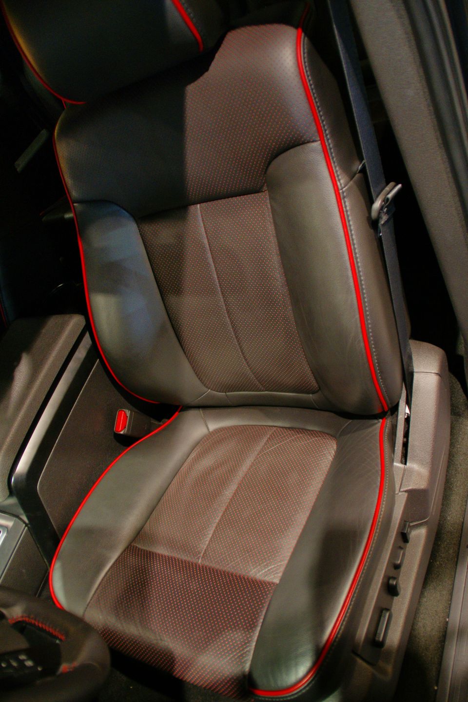 Dark leather car seat with red piping and perforated fabric inserts