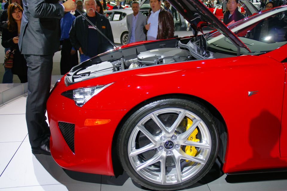 Red sports car with hood open, showing engine and yellow brake calipers. People are looking at it