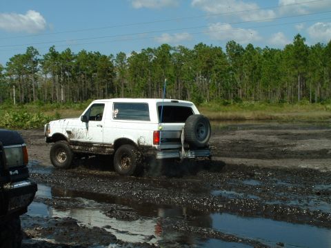 1995 Ford Bronco - A white 1995 Ford Bronco navigates a muddy terrain, kicking up dirt as it goes.