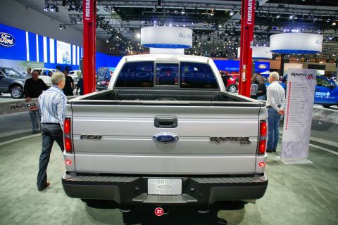 1993 Ford Taurus - Silver Ford F-150 Raptor pickup truck displayed at an auto show with "BUILT TOUGH" on the license plate frame.