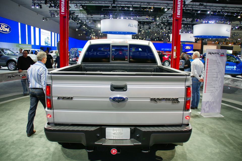Rear view of a silver Ford F-150 Raptor pickup truck at an auto show. "BUILT TOUGH" license plate frame visible