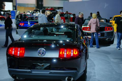 1993 Ford Taurus - A black Ford Mustang is parked at an auto show with other vehicles and people around.
