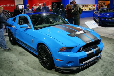 1993 Ford Taurus - A bright blue Ford Mustang with black racing stripes is displayed at an auto show.