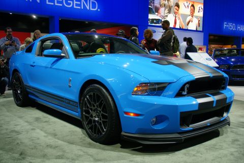1993 Ford Taurus - A blue Ford Mustang Shelby GT500 is showcased at an auto show with other vehicles and people in the background.