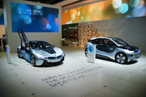 1993 Ford Taurus - Two futuristic concept cars, a BMW i8 and a BMW i3, are displayed at an auto show with informational screens in the background.