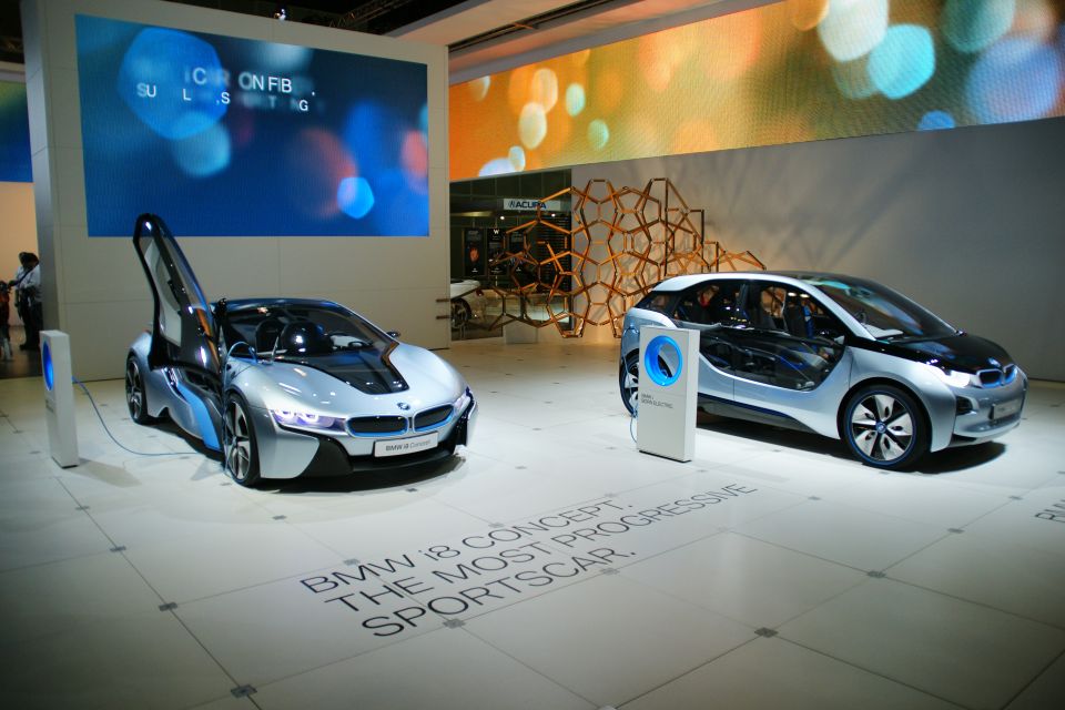 Two concept cars, a silver BMW i8 with dihedral doors open and a silver BMW i3, on display at an auto show
