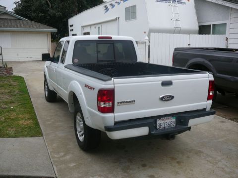 1988 Ford Bronco - A white Ford Ranger pickup truck is parked in a driveway, with another truck and a trailer visible in the background.