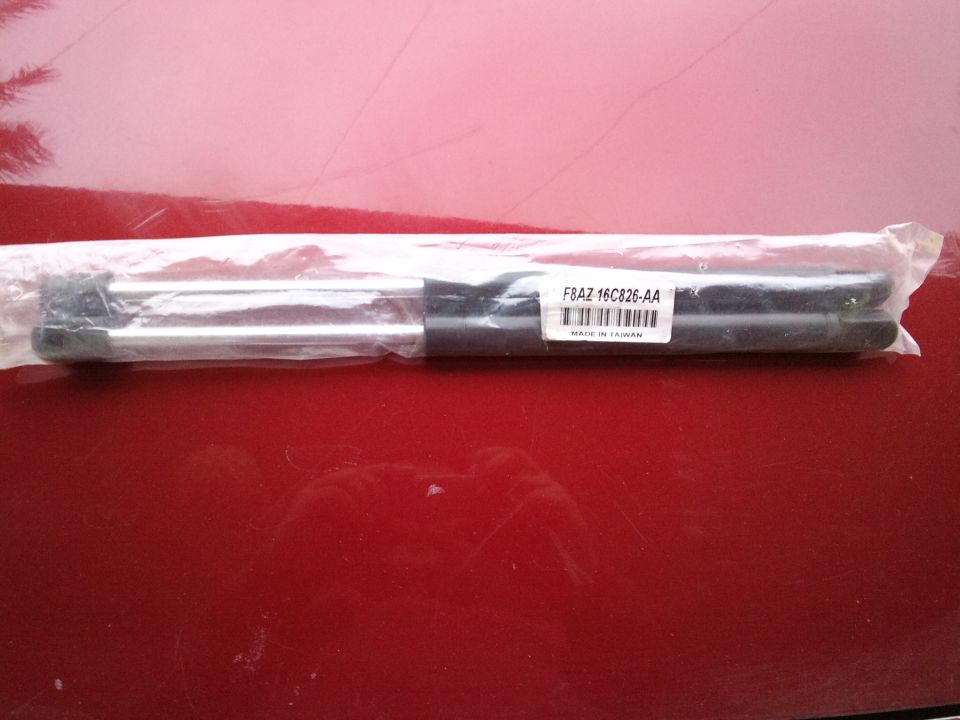 Hood struts in plastic packaging with label F8AZ 16C826-AA on a red surface